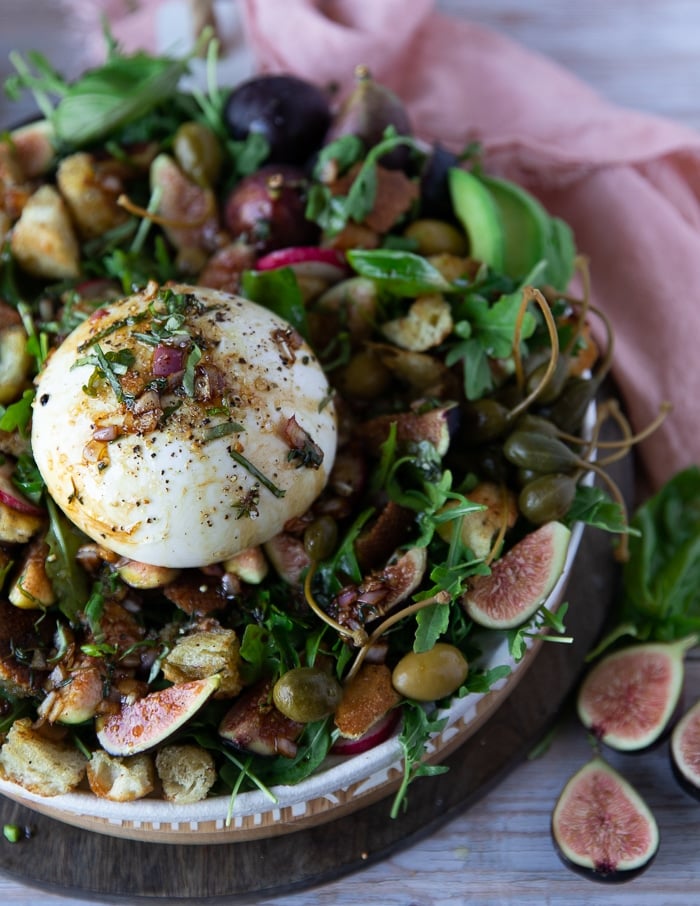 sideview of half a plate of burrata salad showing the entire burrata cheese over the salad