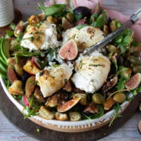 A hand holding a knife and cutting the burrata cheese on the salad