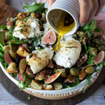 a hand pouring in more dressing over the cut up burrata cheese salad