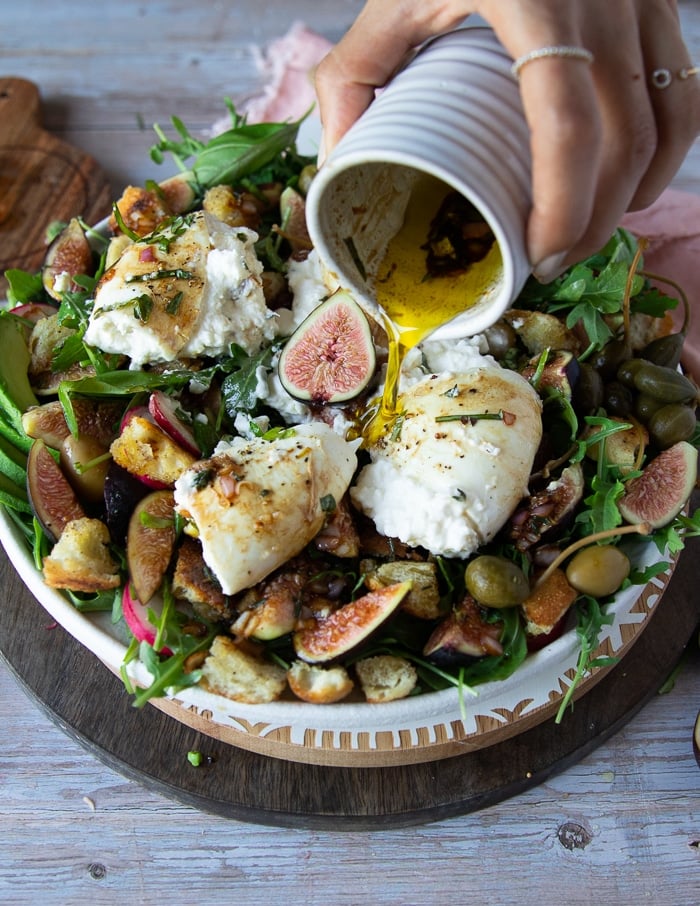 a hand pouring in more dressing over the cut up burrata cheese salad