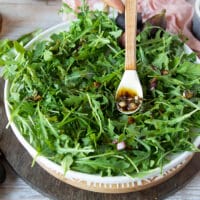 a salad plate with arugula and fresh basil and then a hand pouring in a little bit of dressing to flavor the greens