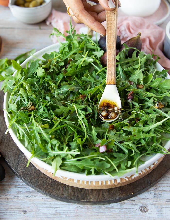a salad plate with arugula and fresh basil and then a hand pouring in a little bit of dressing to flavor the greens