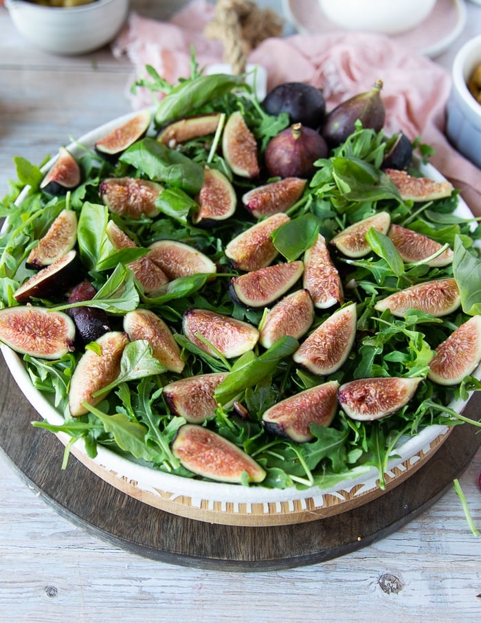 A hand adding the fresh figs over the greens