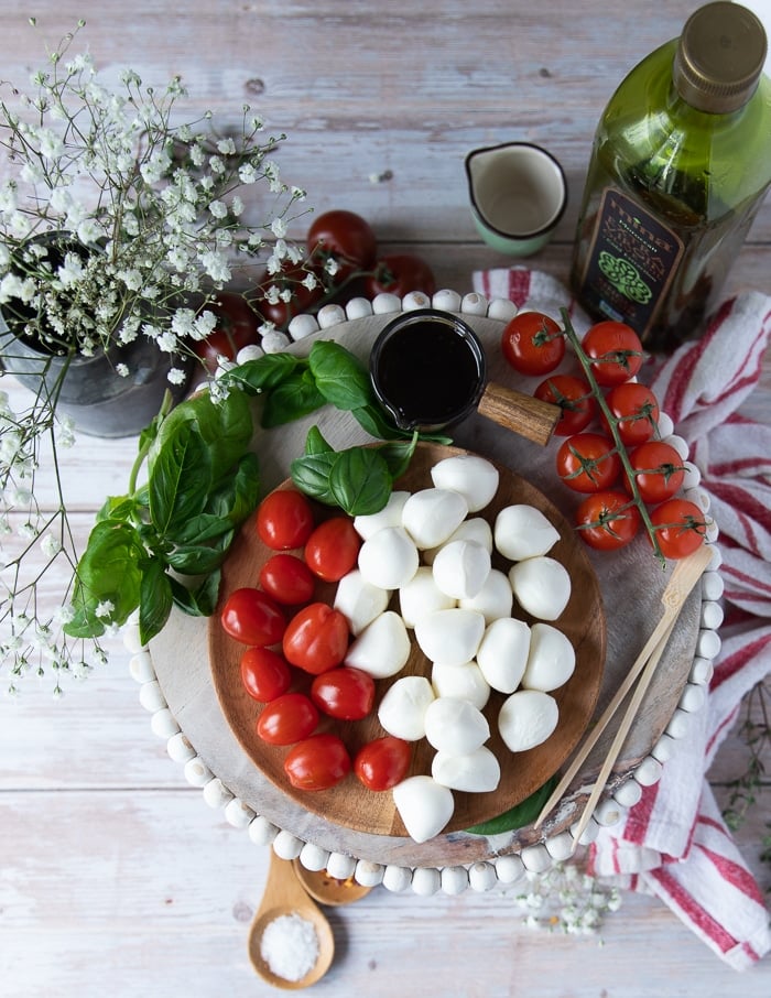 ingredients for caprese skewers on a board including some bocconcini cheese, baby tomatoes, fresh basil