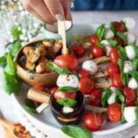 A hand holding a caprese skewer dipped in balsamic glaze