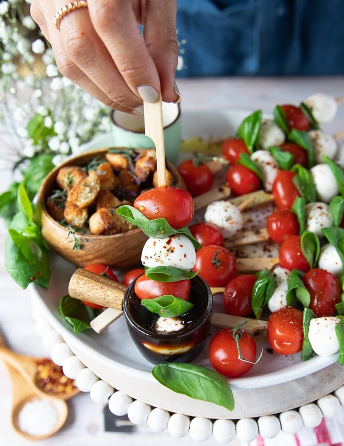 A hand holding a caprese skewer dipped in balsamic glaze