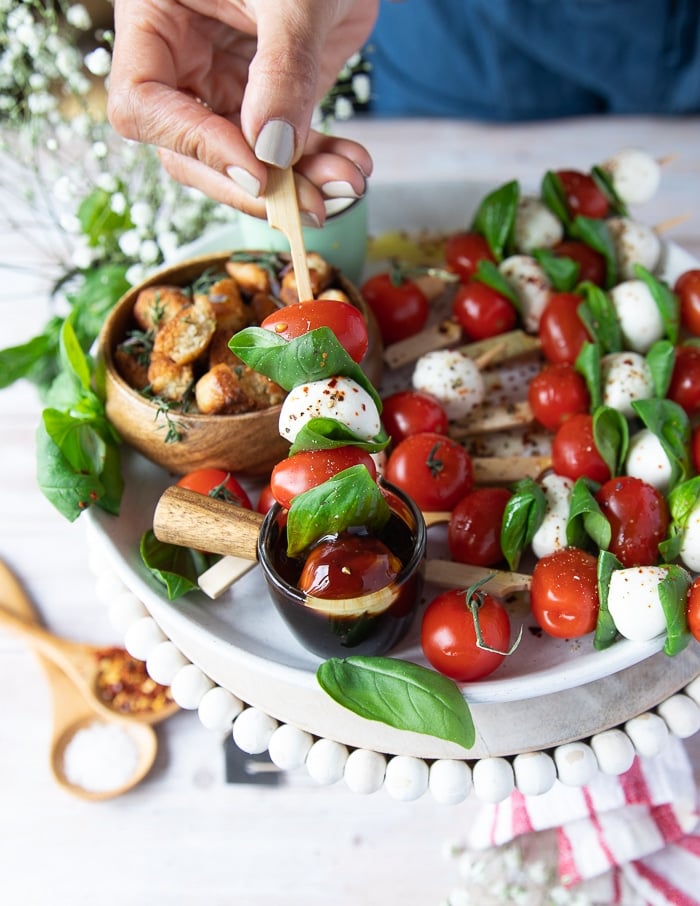 a hand lifting the caprese skewer from the balsamic bowl