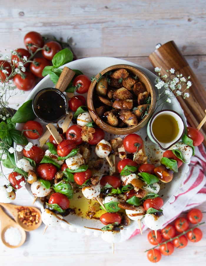 A full plate of caprese skewers drizzled with balsamic glaze, seasoning, olive oil, and crushed croutons