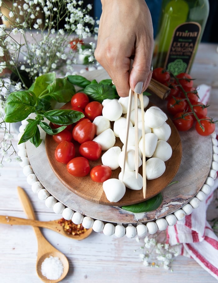 A hand holding wooden skewers for skewering the caprese skewers recipe