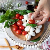 A hand holding a wooden skewer skewering a tomato