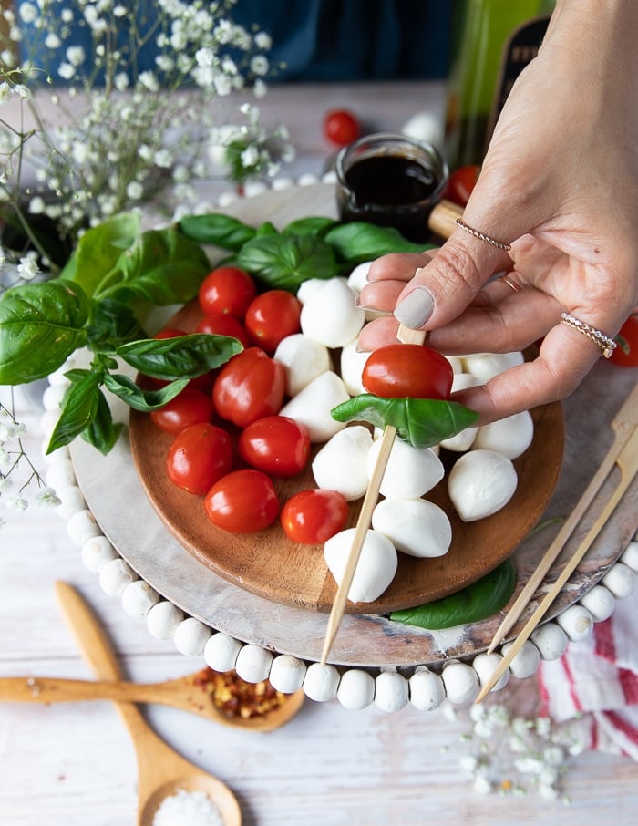 A hand holding a wooden skewer skewering a tomato