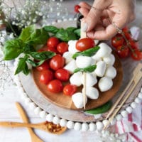 a hand continuing to skewer the cheese and basil with the tomatoes