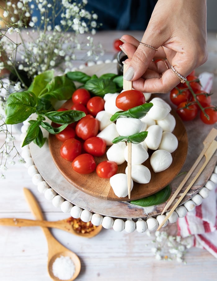 a hand continuing to skewer the cheese and basil with the tomatoes