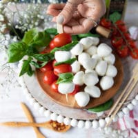 A hand holding one finished skewer of caprese salad