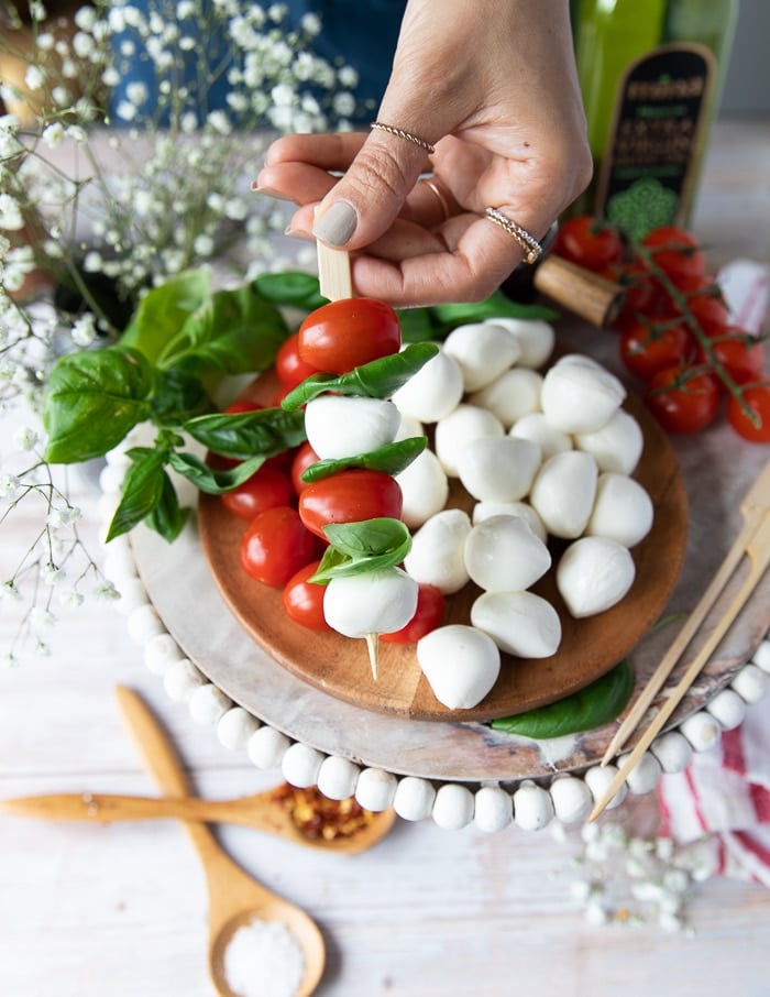 A hand holding one finished skewer of caprese salad