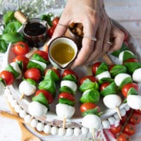 A small jar with olive oil being poured over the caprese skewers