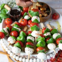 A hand holding a caprese skewer with chilli flakes seasoned with olive oil and salt