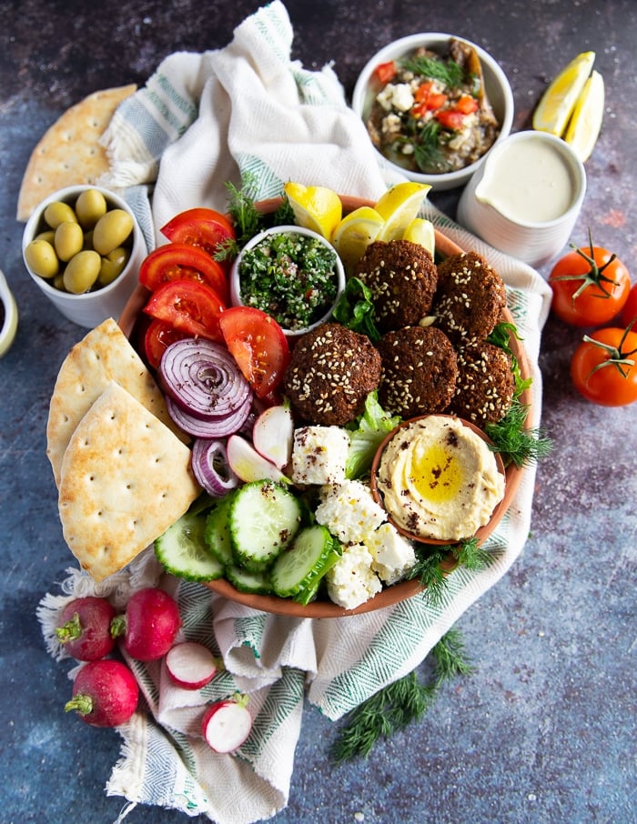 One large falafel bowl with homemade falafel, tahini sauce, tabouleh, fresh veggies, lettuce, olives, onions and bread