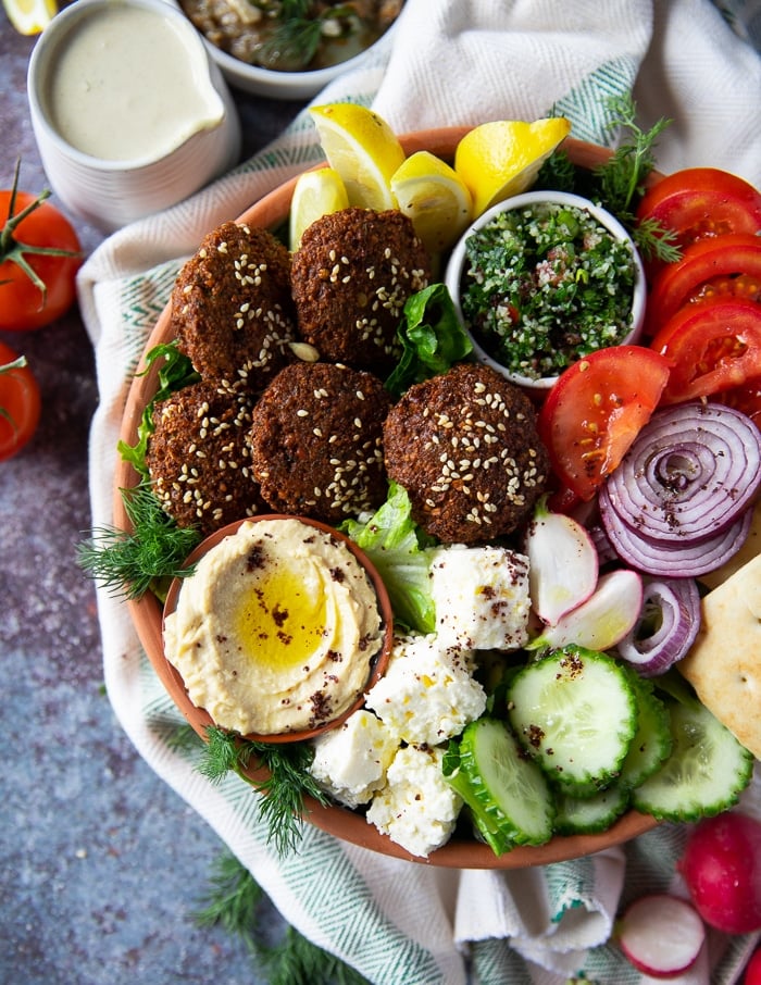 close up if the falafel bowl showing a small plate of hummus next to the falafel, some feta, cucumber, tomatoes, onions, tabouleh and lemon wedges