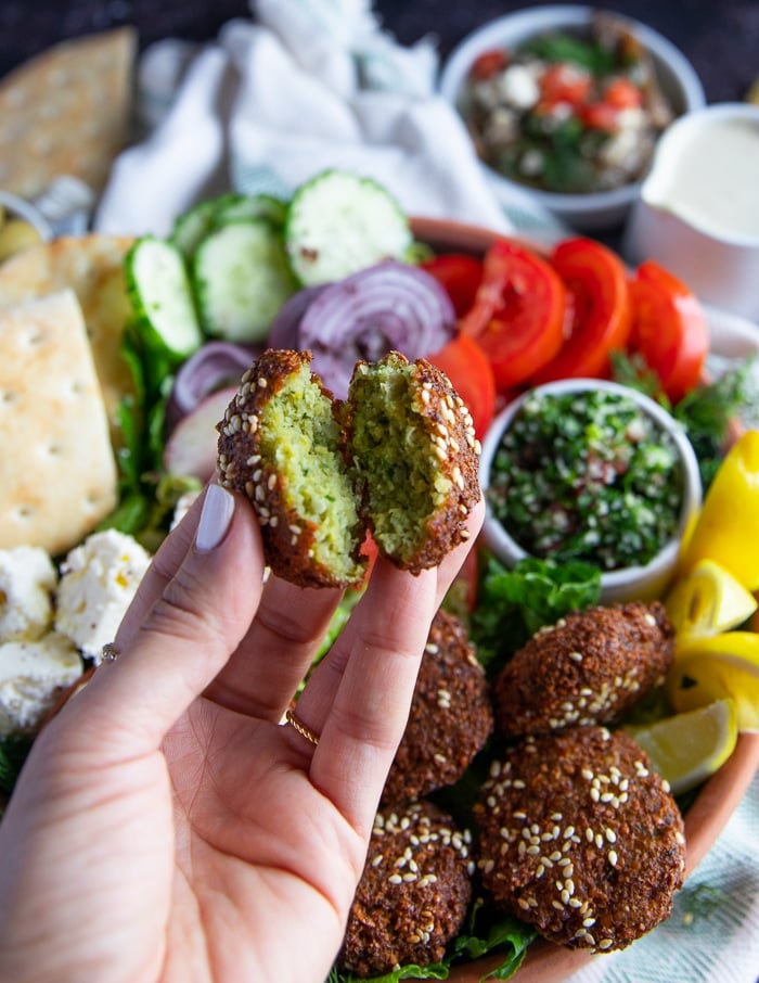 A hand holding a falafel bitten to show how crispy it is and how the inside is so flavorful