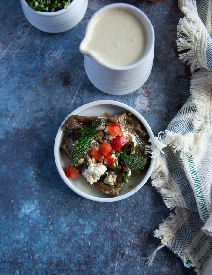 A sauce jar of tahini sauce next to some eggplant salad