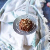 ladle holding up a fried falafel showing the golden crust