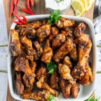 A plate of chicken wings, half with a BBQ sauce and the other half with hot sauce served on a plate with a blue cheese dip on the side and some lemon wedges