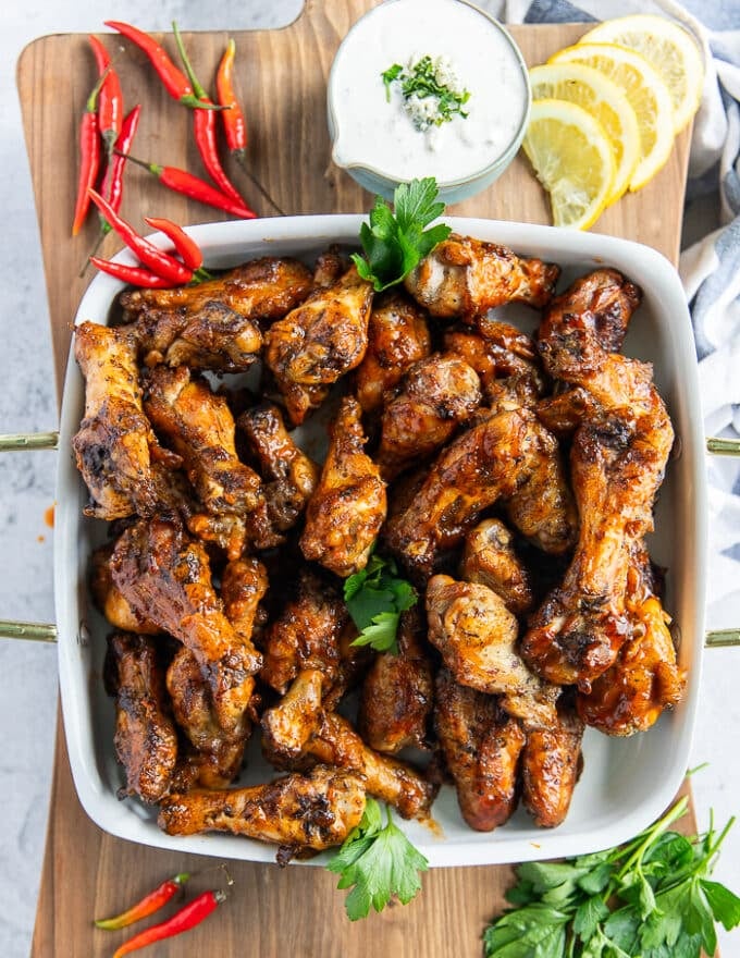 A plate of chicken wings, half with a BBQ sauce and the other half with hot sauce served on a plate with a blue cheese dip on the side and some lemon wedges