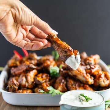 A hand dipping grilled chicken wings into blue cheese sauce and showing the perfectly grilled chicken wings