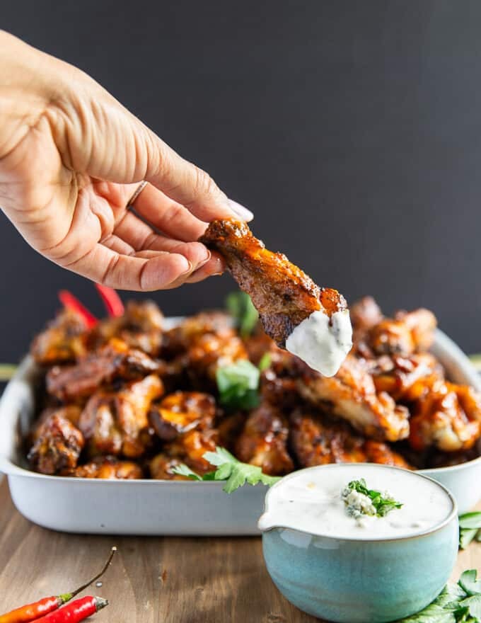 A hand dipping grilled chicken wings into blue cheese sauce and showing the perfectly grilled chicken wings
