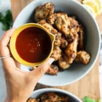 grilled chicken wings divided into two separate bowls, this is the BBQ bowl with a hand pouring in the BBQ sauce over the wings