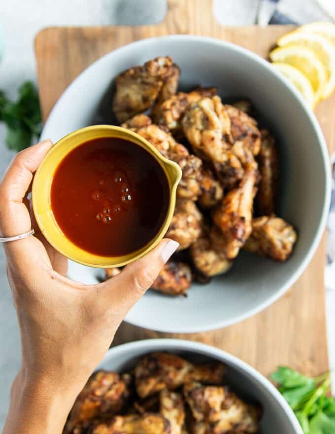 grilled chicken wings divided into two separate bowls, this is the BBQ bowl with a hand pouring in the BBQ sauce over the wings