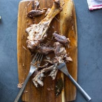 the erady cooked lamb on a cutting board being shredded by two forks