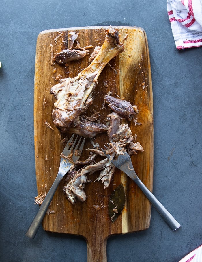 the erady cooked lamb on a cutting board being shredded by two forks