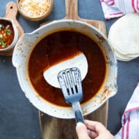 the tortillas are being dipped into the birria stew sauce before searing