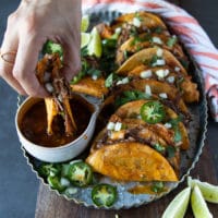 A hand dipping a lamb birria into the birria sauce