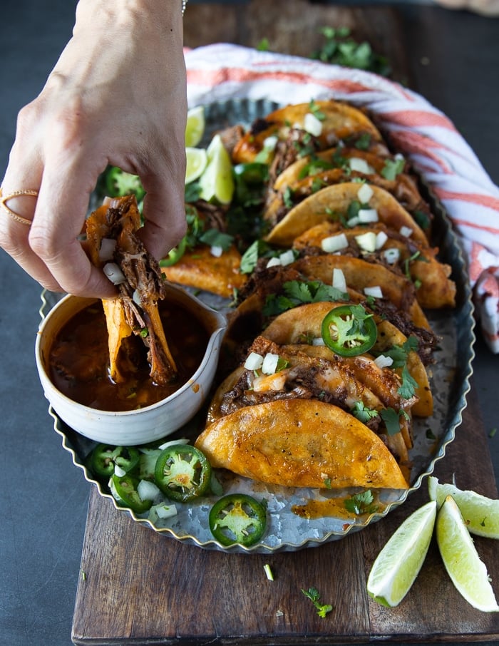 A hand dipping a lamb birria into the birria sauce