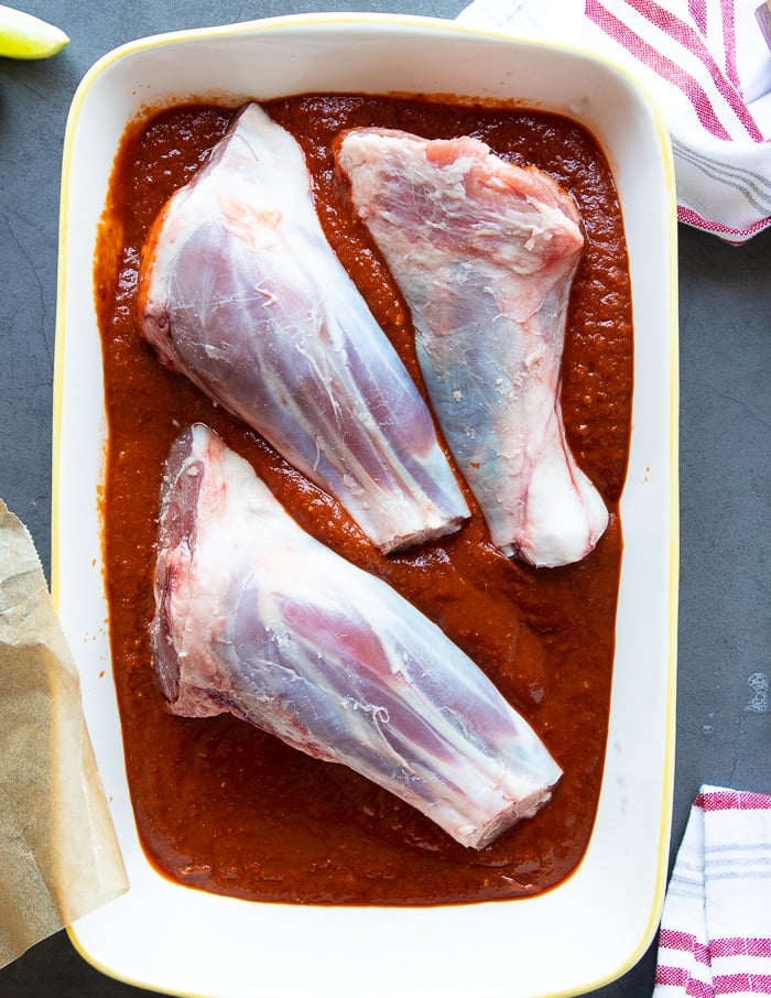 lamb shanks in a large dish marinating in the birria sauce