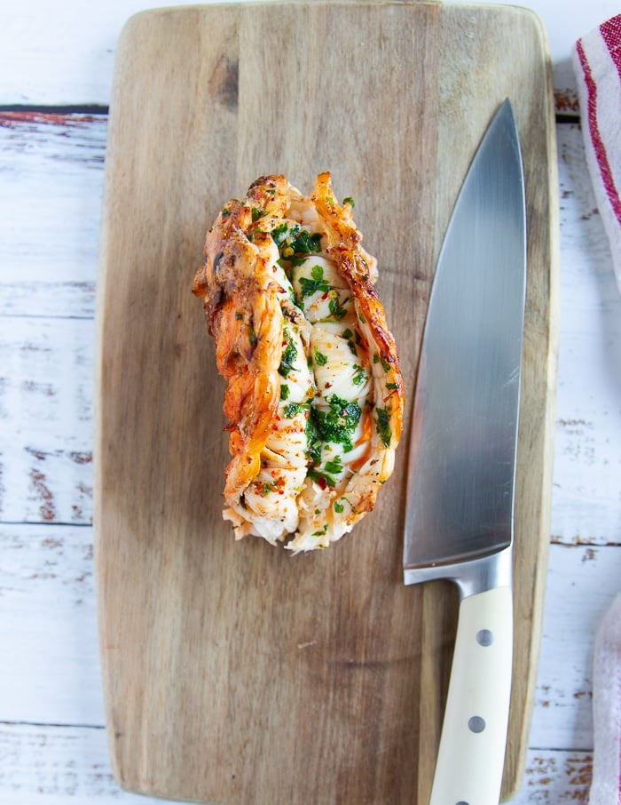 A whole cooked lobster tail on a cutting board 