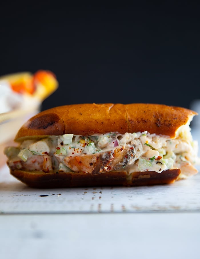 A bitten lobster roll on a wooden board showing the rich lobster filling and the fluffy toasted bun 
