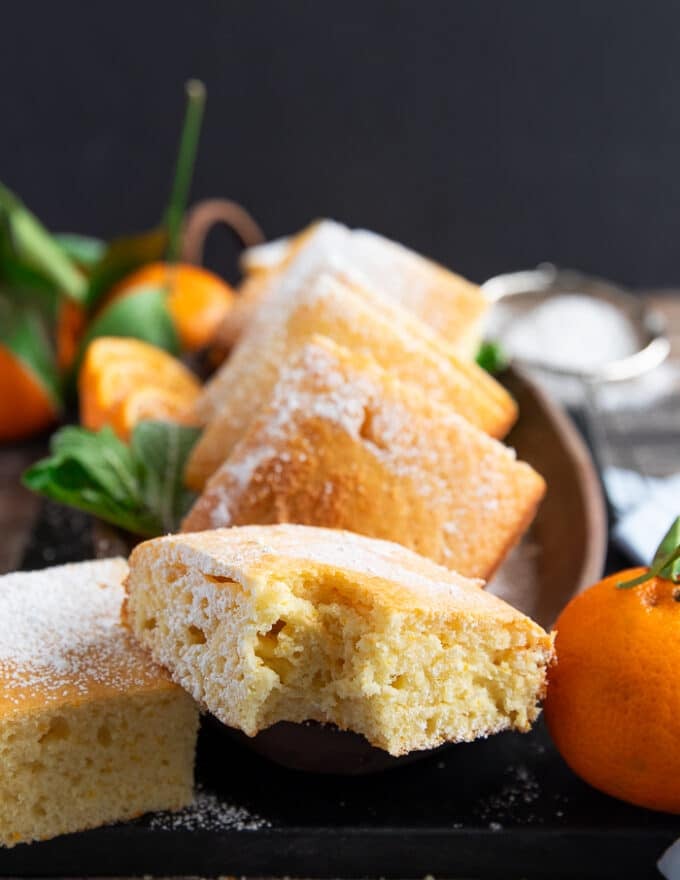 A piece of bitten up mandarin orange cake on a wooden board