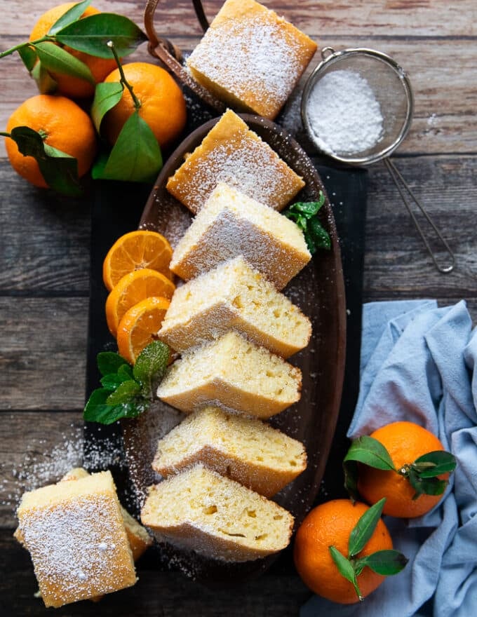 Top view of a plate of cut up mandarin orange cake with orange slices, and mandarin orange around it