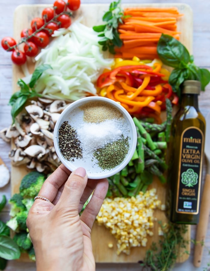 All of the ingredients for pasta primavera: salt, pepper, oregano, garlic, basil, and spring veggies plus cooked pasta.