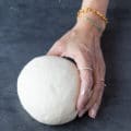 Best Pizza Dough Recipe Ever! Rolled ball of dough held by human hand.