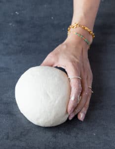 Best Pizza Dough Recipe Ever! Rolled ball of dough held by human hand.