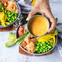 A hand pouring some spicy mayo over the salmon sushi bowl