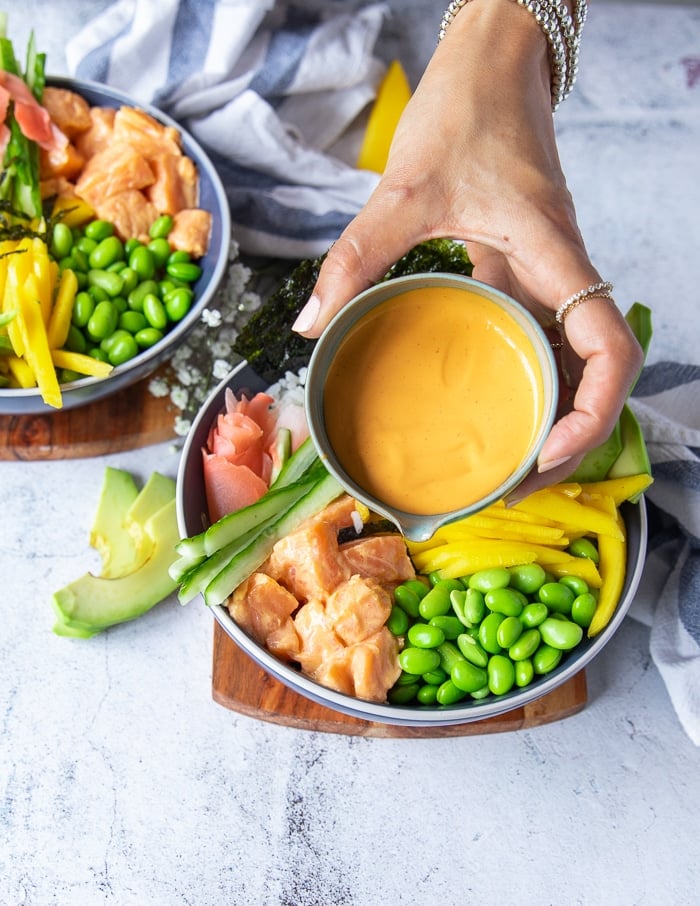 A hand pouring some spicy mayo over the salmon sushi bowl