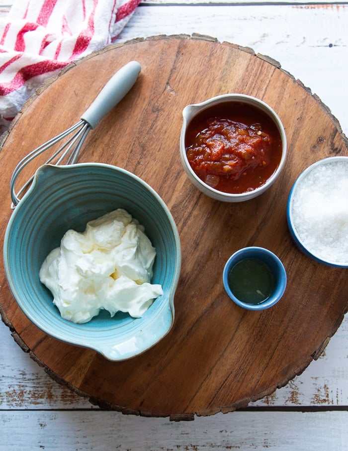 ingredientes de aderezo para ensalada de tacos en una tabla de madera que incluye un tazón de crema agria, un tazón de salsa, jugo de lima y ensalada