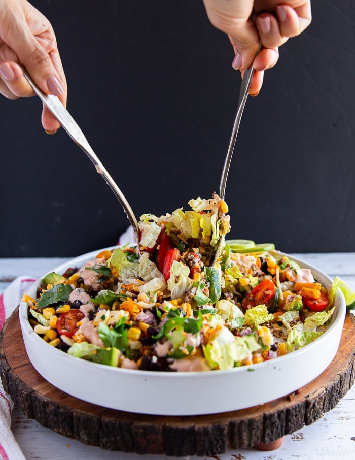 A hand with two spoons serving the taco salad