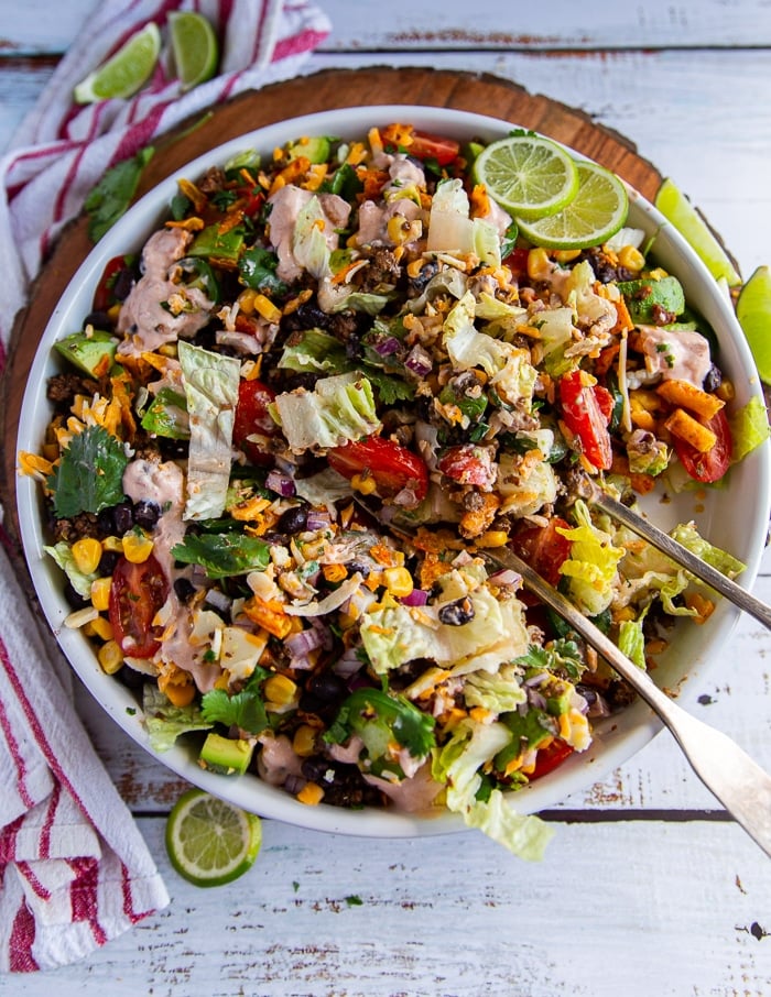 large plate of taco salad with two serving spoons all mixed up and some it spooned out